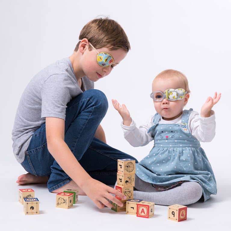 Wearing reusable eye patches – a boy and baby playing with toy blocks