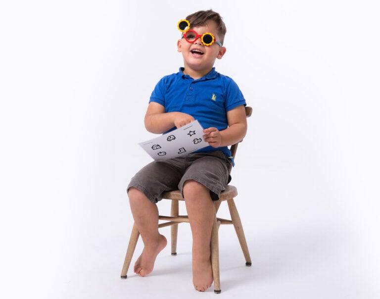 Boy wearing sunflower flip-up occluding glasses, sitting on a stool pointing at the Kay Picture Test Matching Card